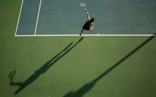 Tennis player serving under dramatic arena lights, illustrating Ben Shelton's comments