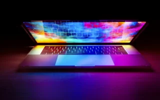 M6 MacBook Pro style laptop glowing in a dark room