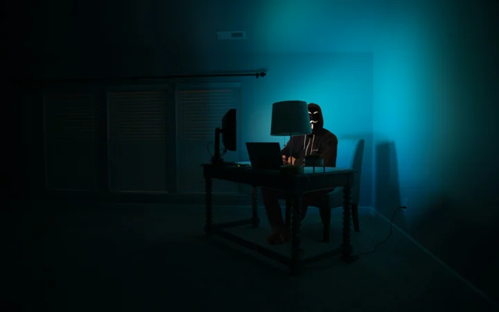Hooded figure lit by a dark screen, illustrating the ROMULUS ClickFix platform malware campaign